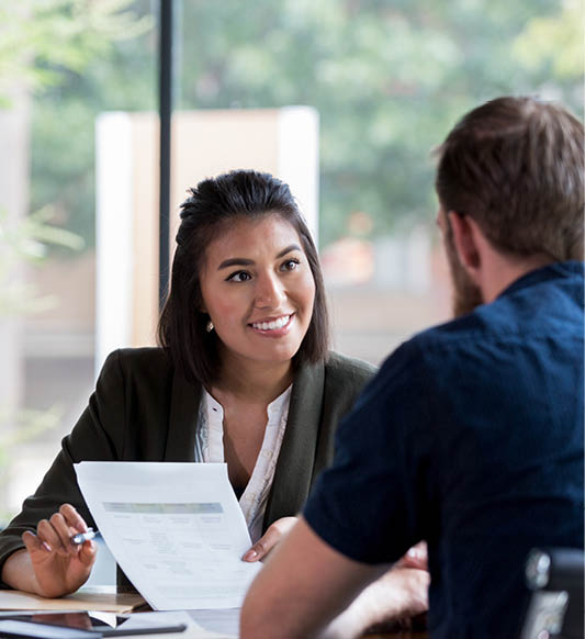 Hispanic businesswoman smiles while showing a document to a male associate.