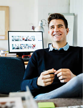 Office working smiling looking off camera with computer behind him