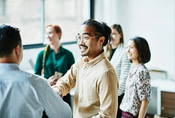 Co-workers shaking hands in a social setting with a group of people
